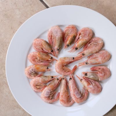 Frozen pink small shrimp prawns lobster on a white plate. Delicious food appetizer, seafood sea food defrosted Raw small pink shrimp in shell with head and tail