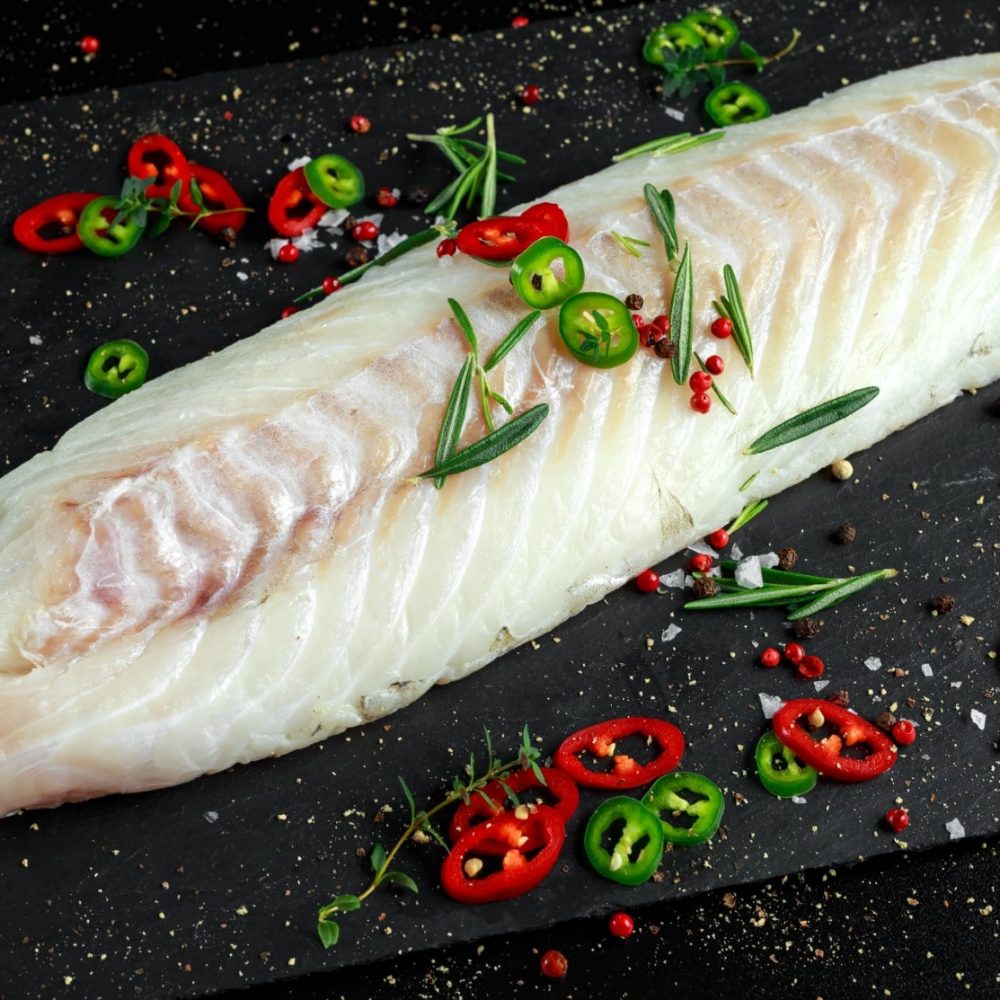 Fresh Raw Cod loin fillet with rosemary, chillies, cracked pepper on stone board