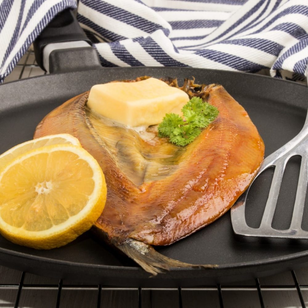 smoked kipper with lemon, butter and parsley on a pan